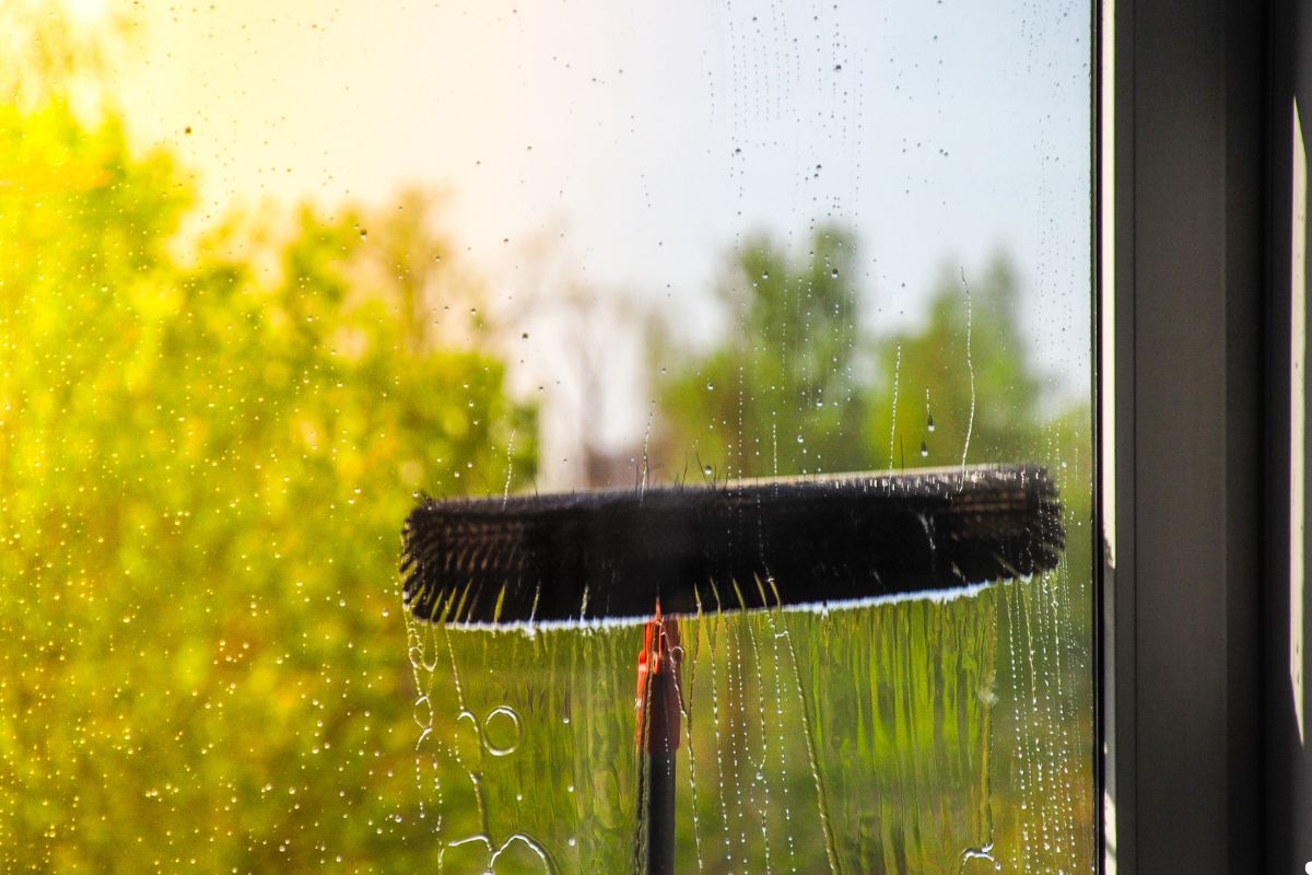A window with a cleaning brush and a bottle of window cleaner placed on the sill, ready for cleaning.