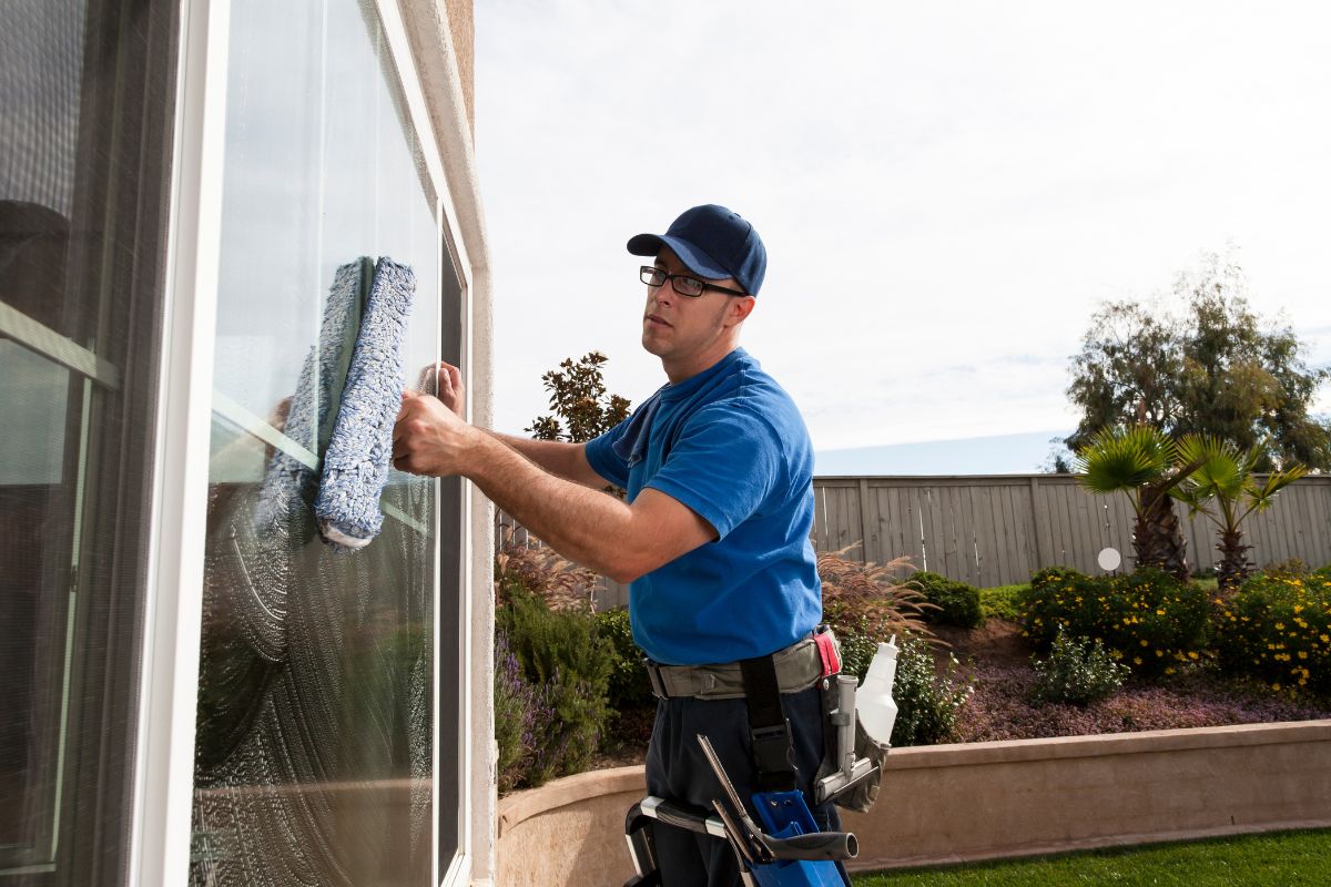 A man in a blue shirt uses a squeegee to clean windows, enhancing the home's curb appeal and value.