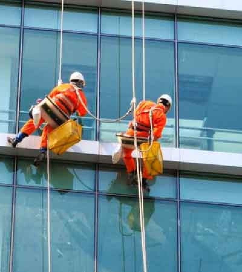 Two workers in orange uniforms performing window washing on a building's exterior, emphasizing business window cleaning.