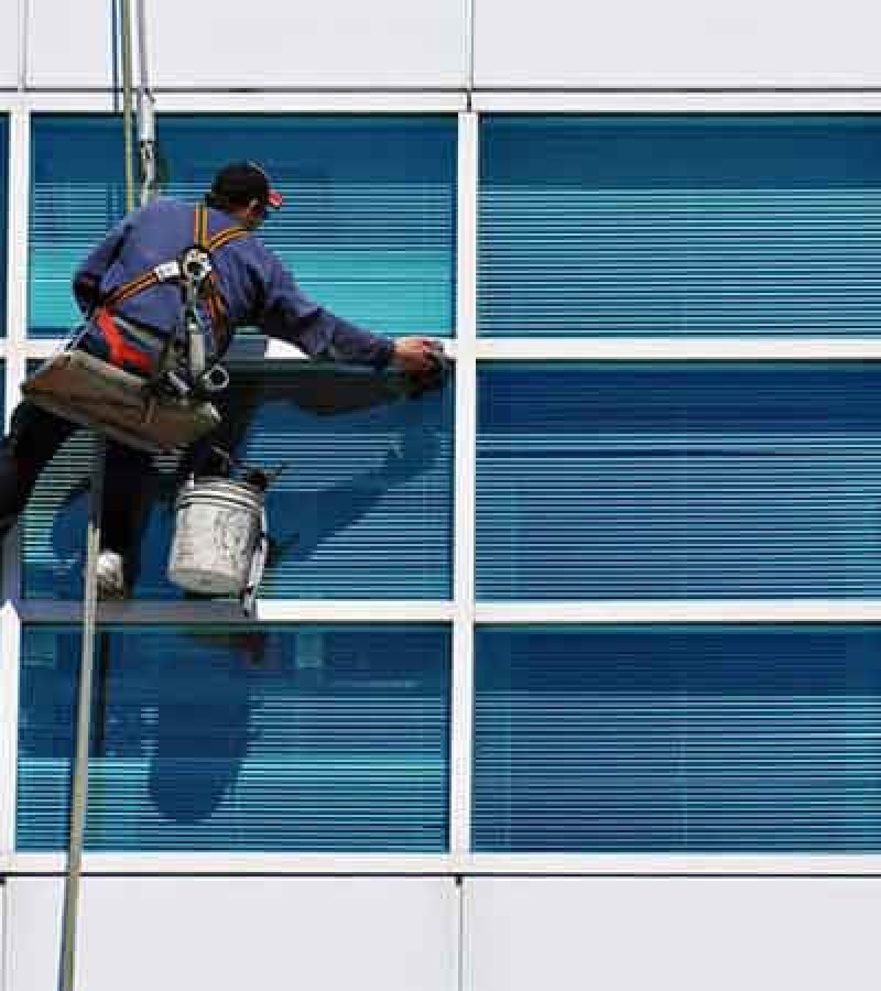 A man stands on a window washing machine, performing elevated window cleaning for a pristine appearance.