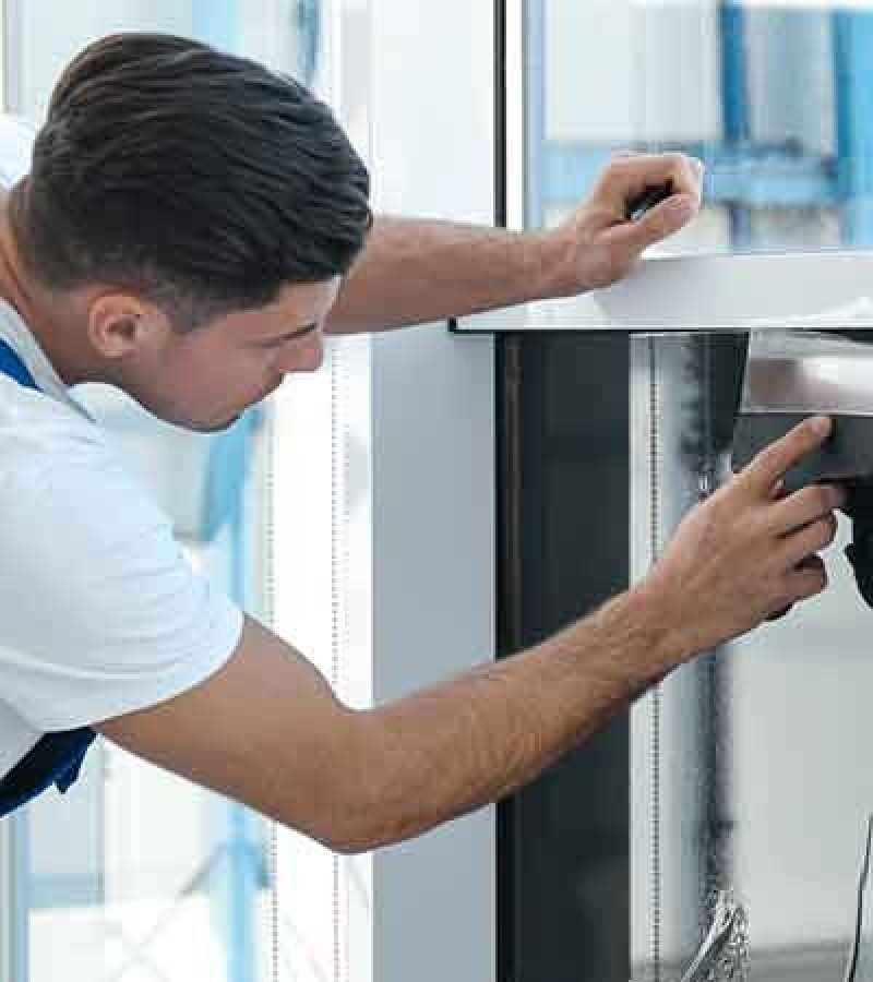 A man in overalls is seen applying a protective coating to a glass window, focusing on quality and precision.